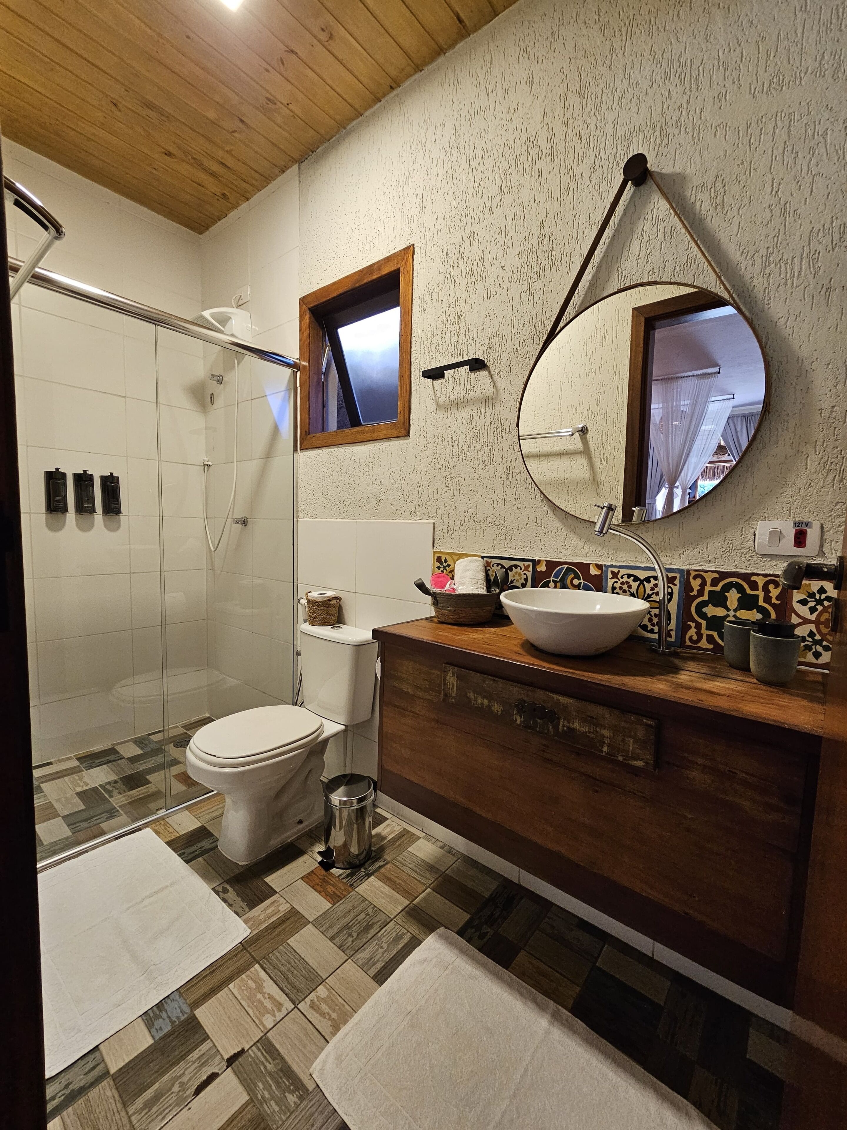 Baño con ducha, inodoro, tocador y un espejo grande.