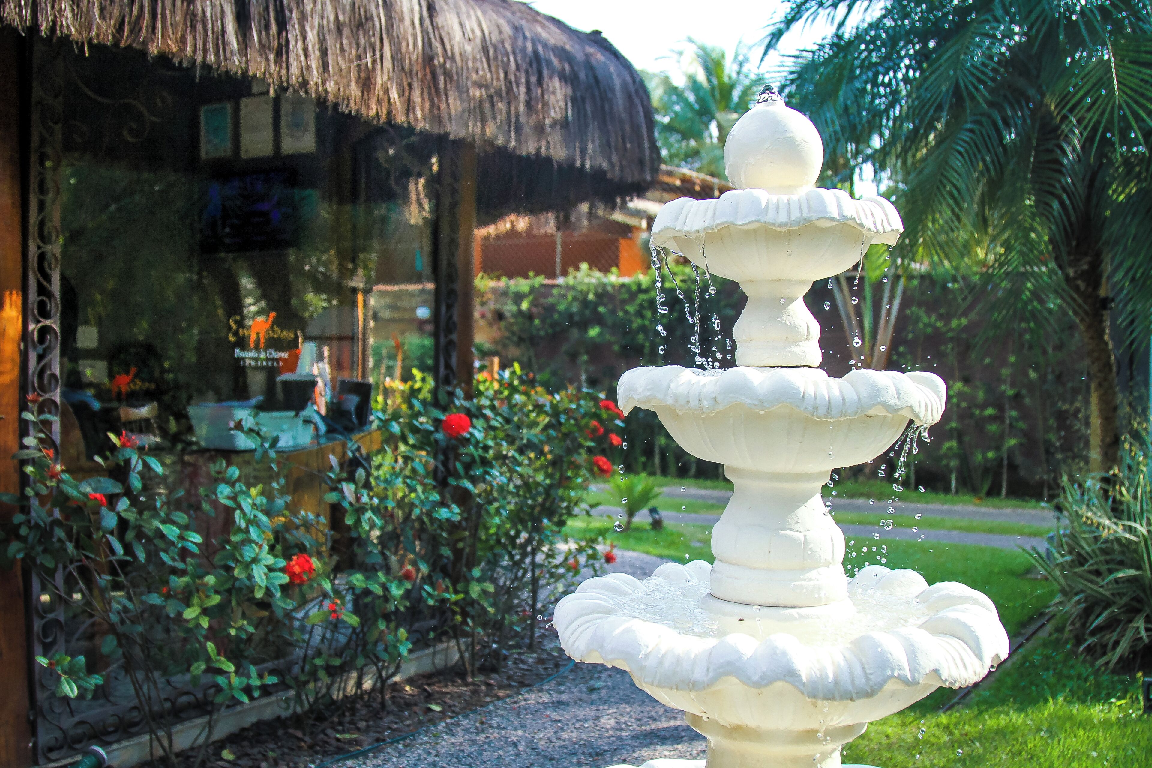 Una fuente escalonada en un jardín con una estructura de techo de paja al fondo.