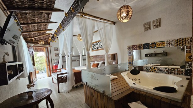 A spacious room with a large bed, a wooden table, a bathtub, and a shower area. - Pousada de Charme Emirados (Ilhabela)