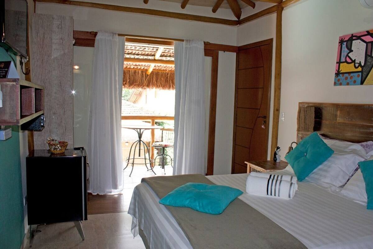 A bedroom with a bed, a small table, a chair, and a view of the outside.
