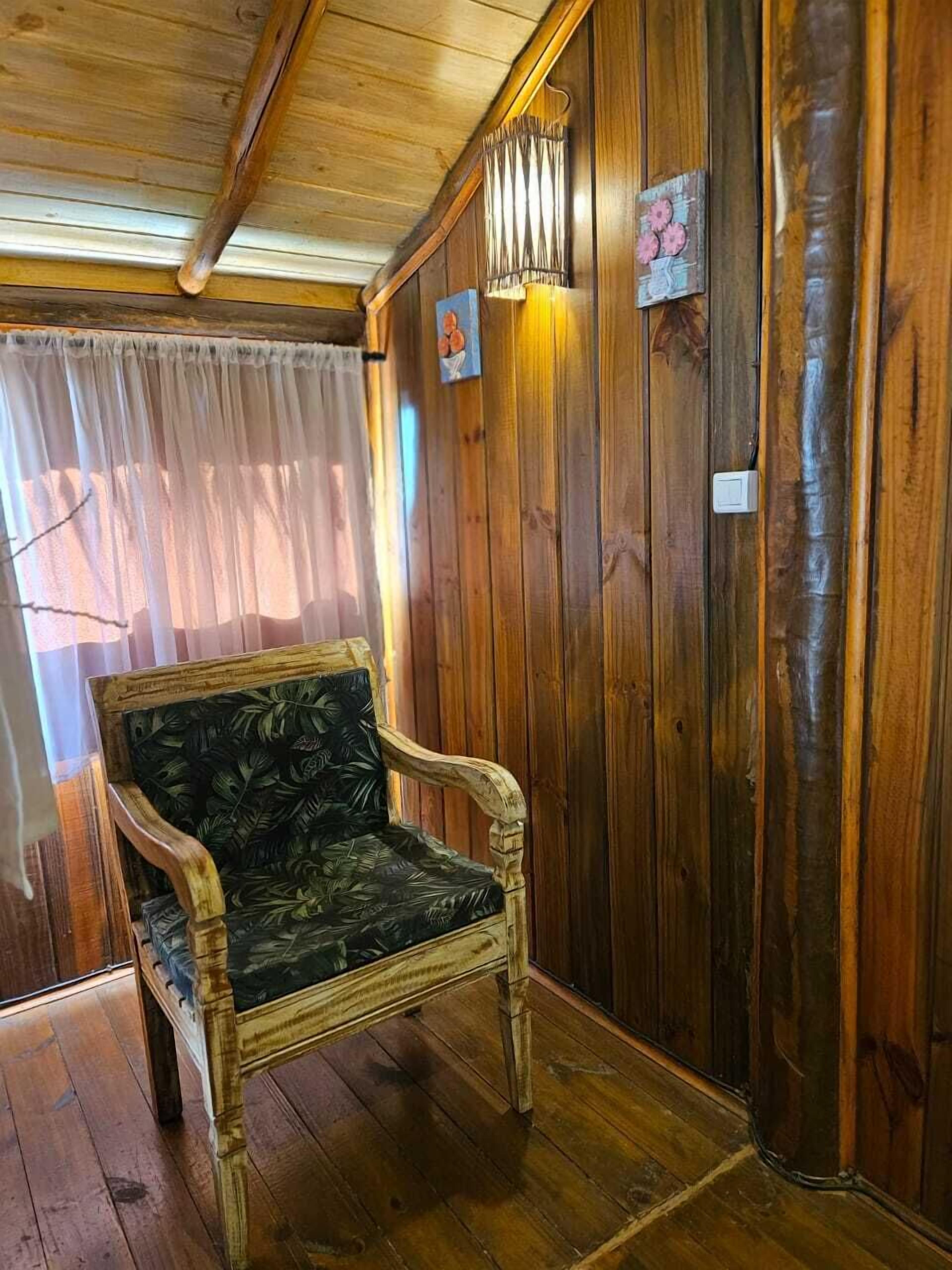 Una habitación con paneles de madera, una sola silla, un aplique de pared y un pequeño marco de fotos.