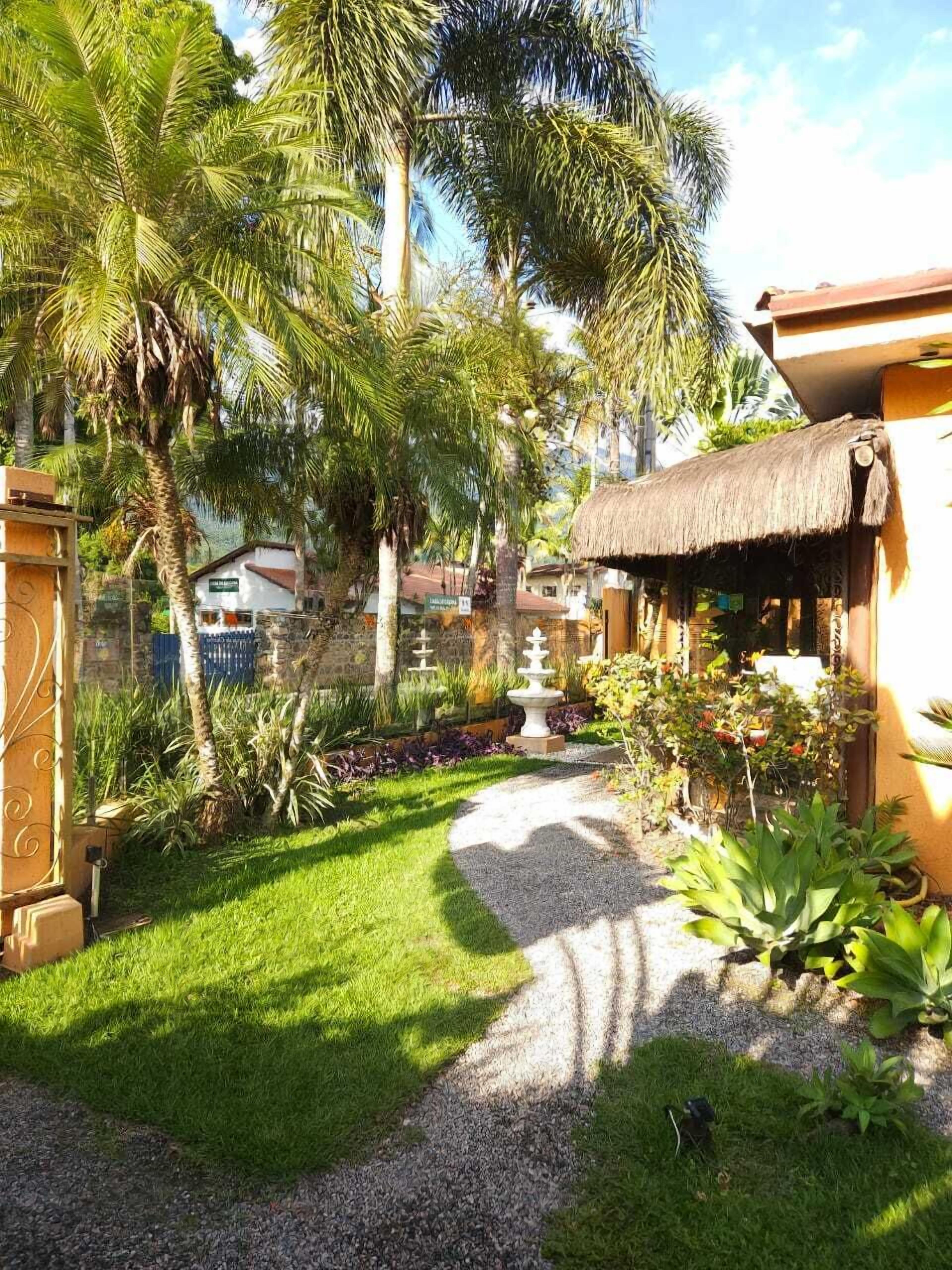 Un jardín con una estructura de techo de paja, palmeras y un camino de grava.