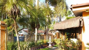 Un jardín con una estructura de techo de paja, palmeras y un camino de grava.