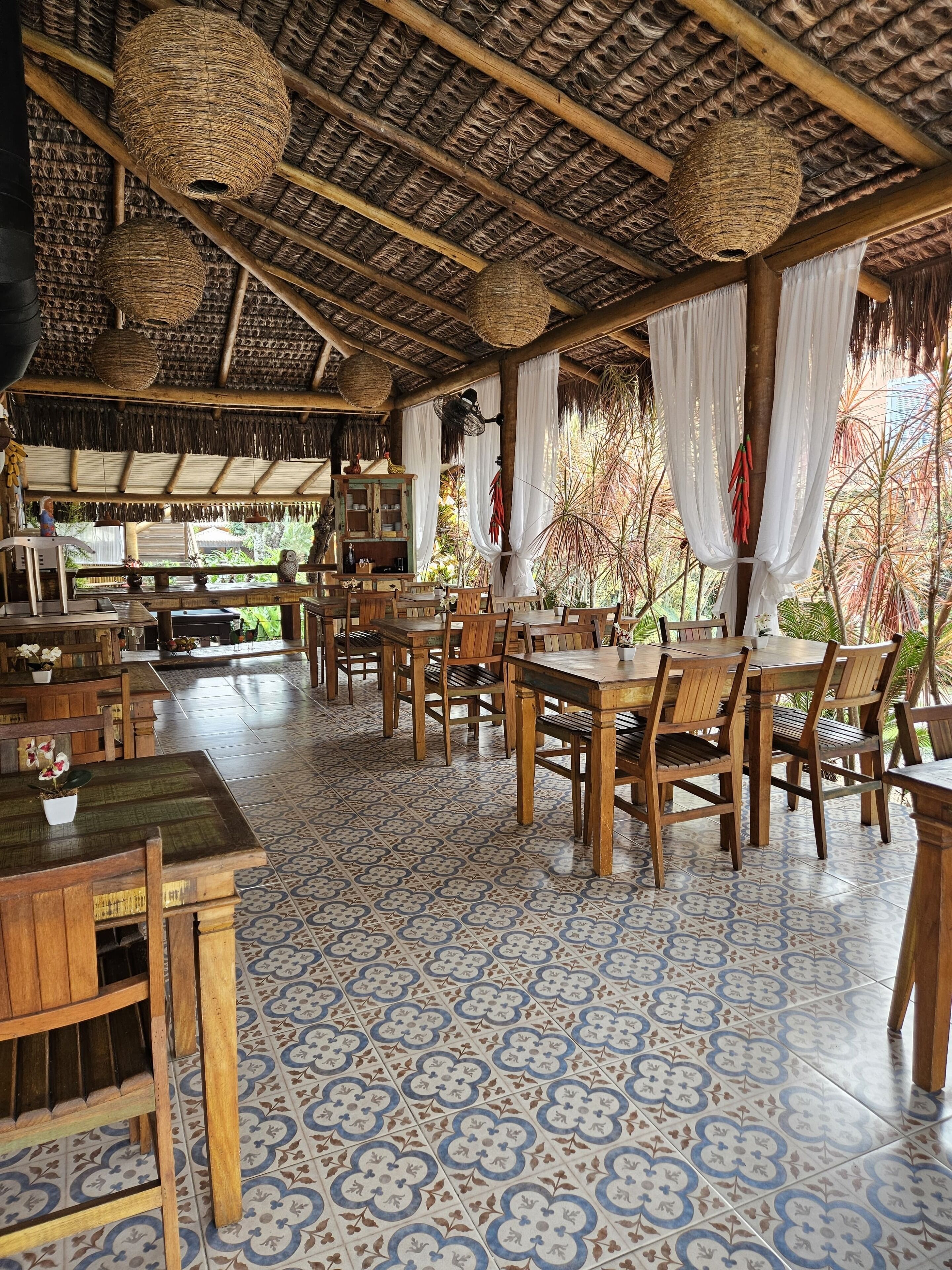 Un restaurante con mobiliario de madera, baldosas de suelo estampadas y techo de paja.