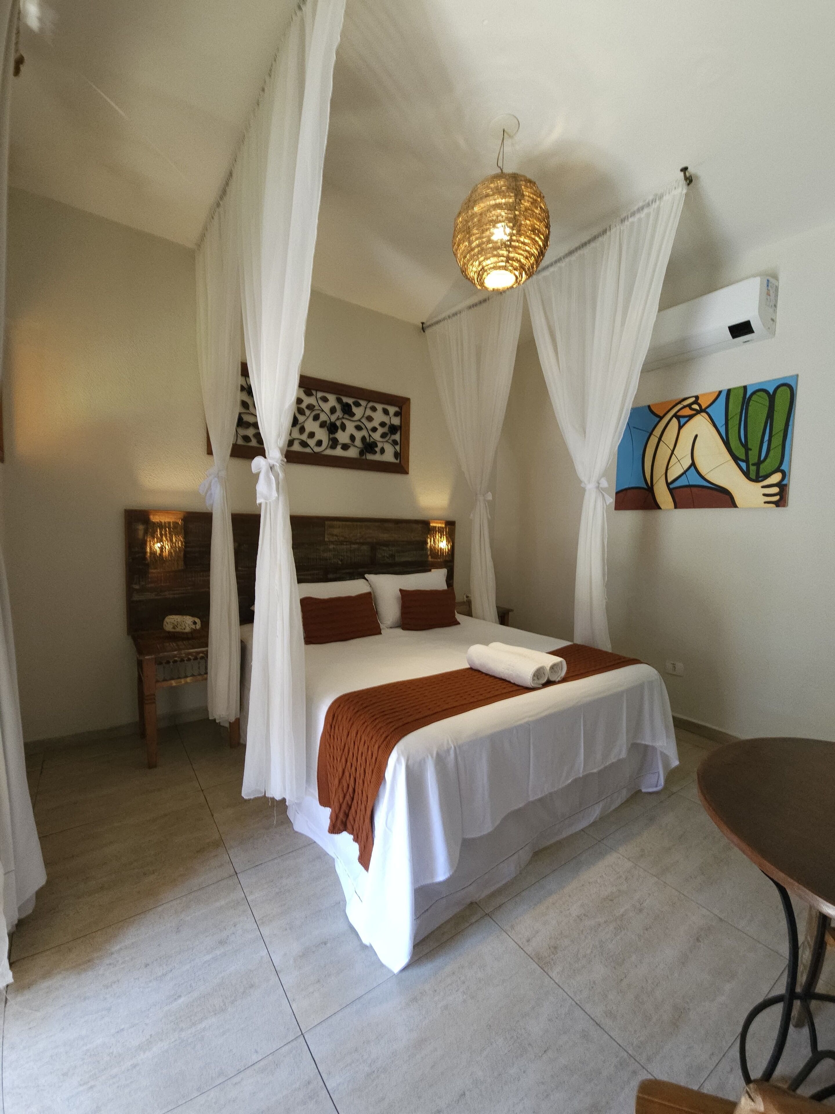 Un dormitorio con una cama, cortinas blancas, un cuadro y un ventilador de techo.