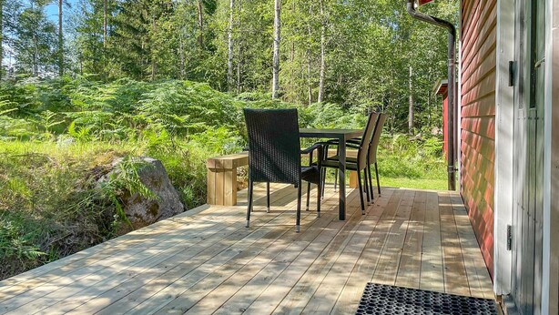 Um deck de madeira com mesa e cadeiras, cercado por vegetação exuberante e árvores.