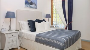 A bedroom with a bed, two bedside tables, a nightstand, a window with curtains, and a painting on the wall. - Burrows (Ottery St Mary)