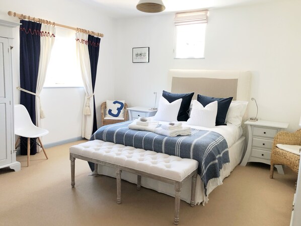 A bedroom with a bed, a bench, a chair, a nightstand, and a small table.