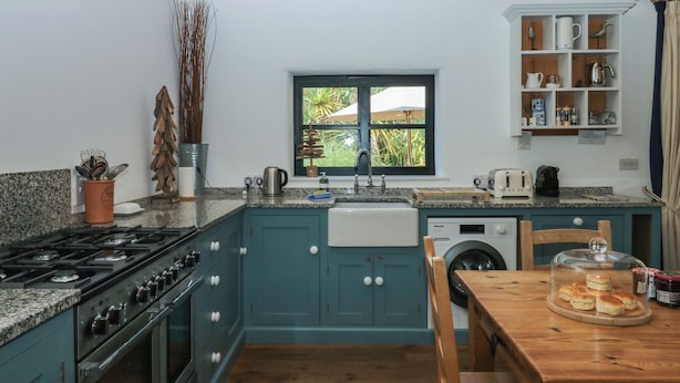 A kitchen with teal cabinets, a stove, a sink, and a window overlooking greenery. - Burrows (Ottery St Mary)