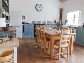 Una cocina con una mesa y sillas de madera, un reloj en la pared y un ventanal con vistas al exterior.