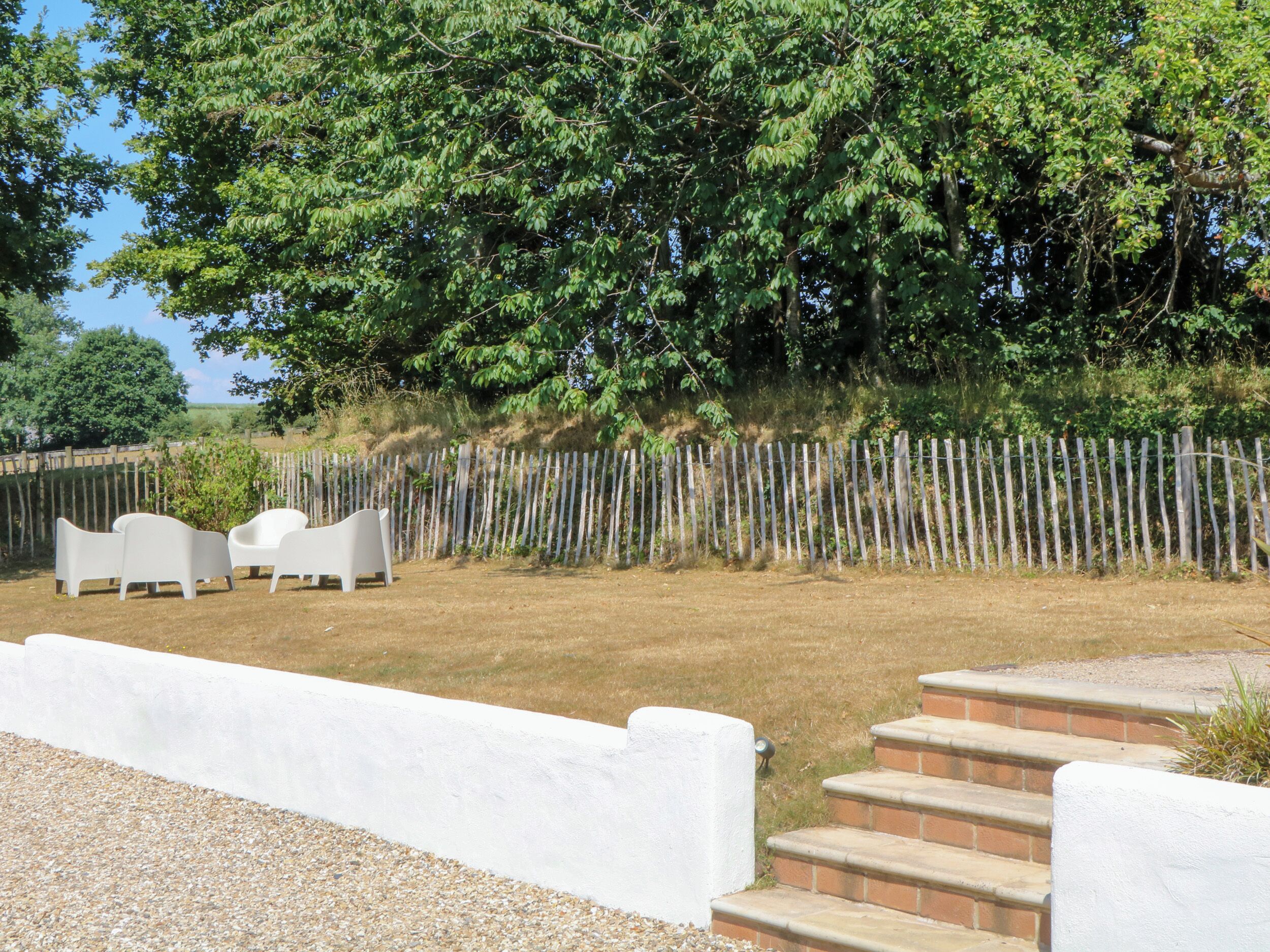 An outdoor seating area with white chairs and a table, surrounded by a wooden fence and trees.