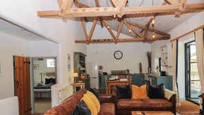 A cozy living room with a wooden ceiling, leather sofas, a wooden coffee table, and a kitchen in the background. - Burrows (Ottery St Mary)