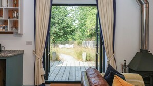 A cozy room with a wooden bench, a fireplace, and a view of a garden through a glass door. - Burrows (Ottery St Mary)
