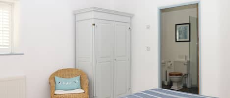 A bedroom with a bed, a wardrobe, a wicker chair, and a bathroom visible through an open door.
