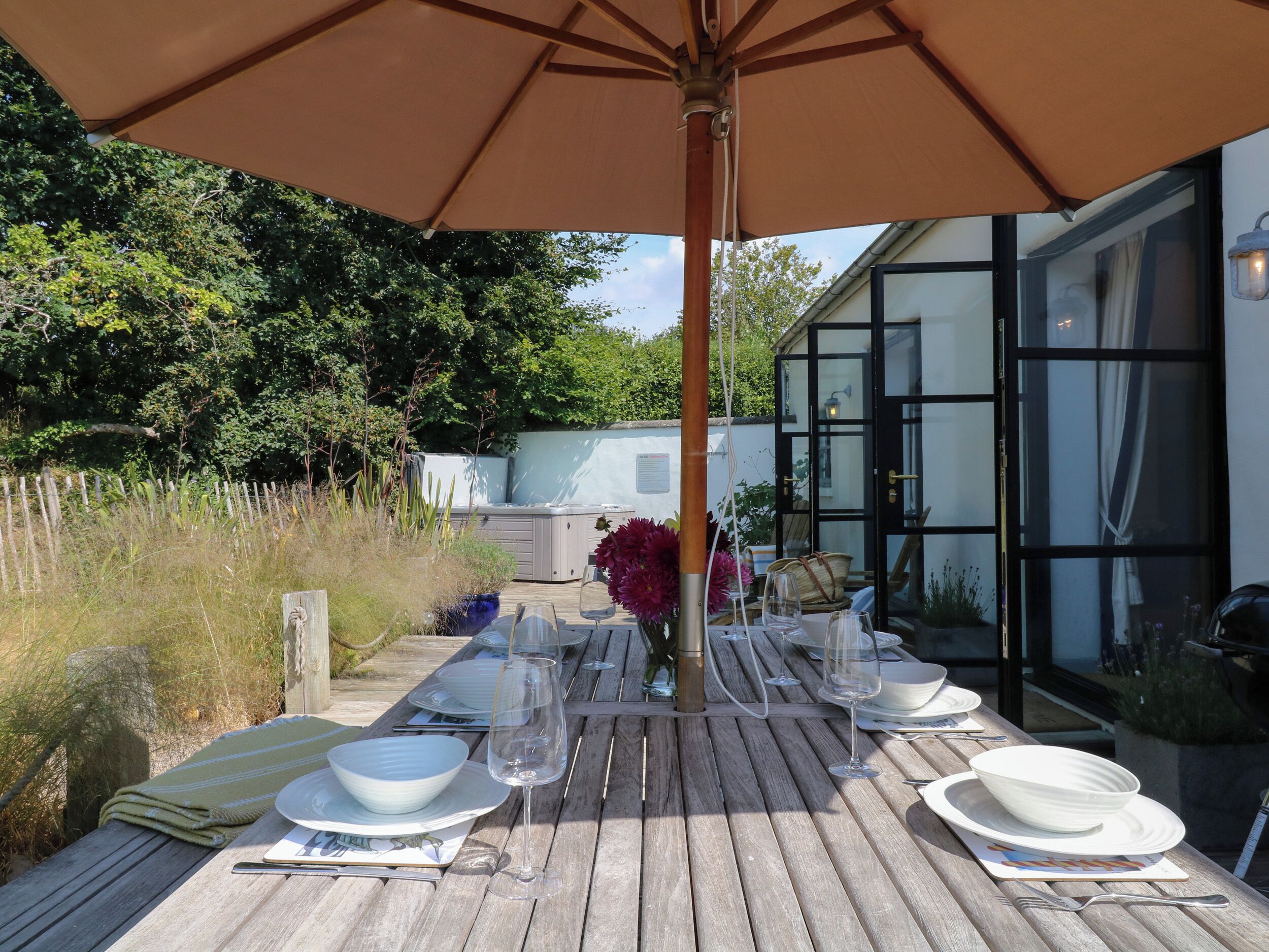 An outdoor dining area with a wooden table set for two, under a large umbrella.