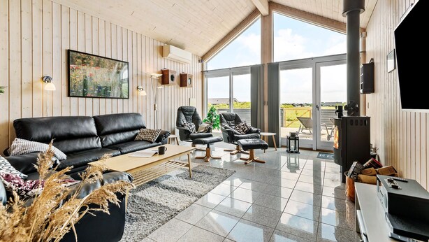 Un salon moderne avec un canapé en cuir noir, deux fauteuils en cuir, une table basse et une grande fenêtre donnant sur l’extérieur.