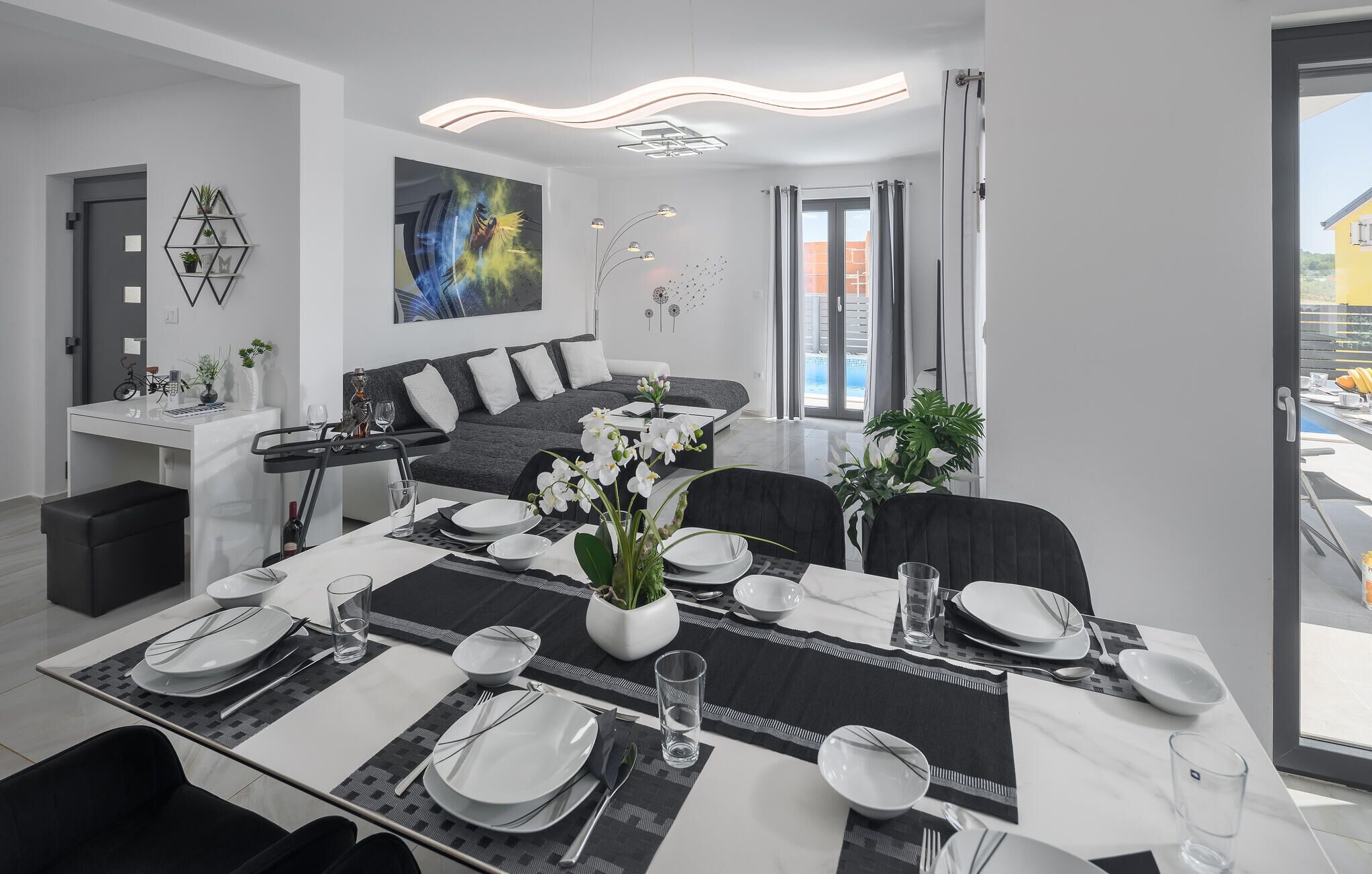 Un espace repas moderne avec une table dressée pour quatre personnes, un canapé et un tableau accroché au mur.