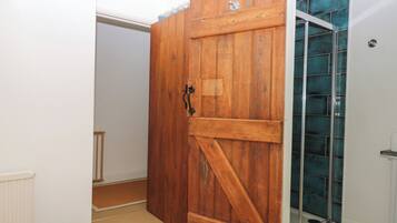 Une pièce avec une porte en bois, un espace de douche en verre et un radiateur blanc.