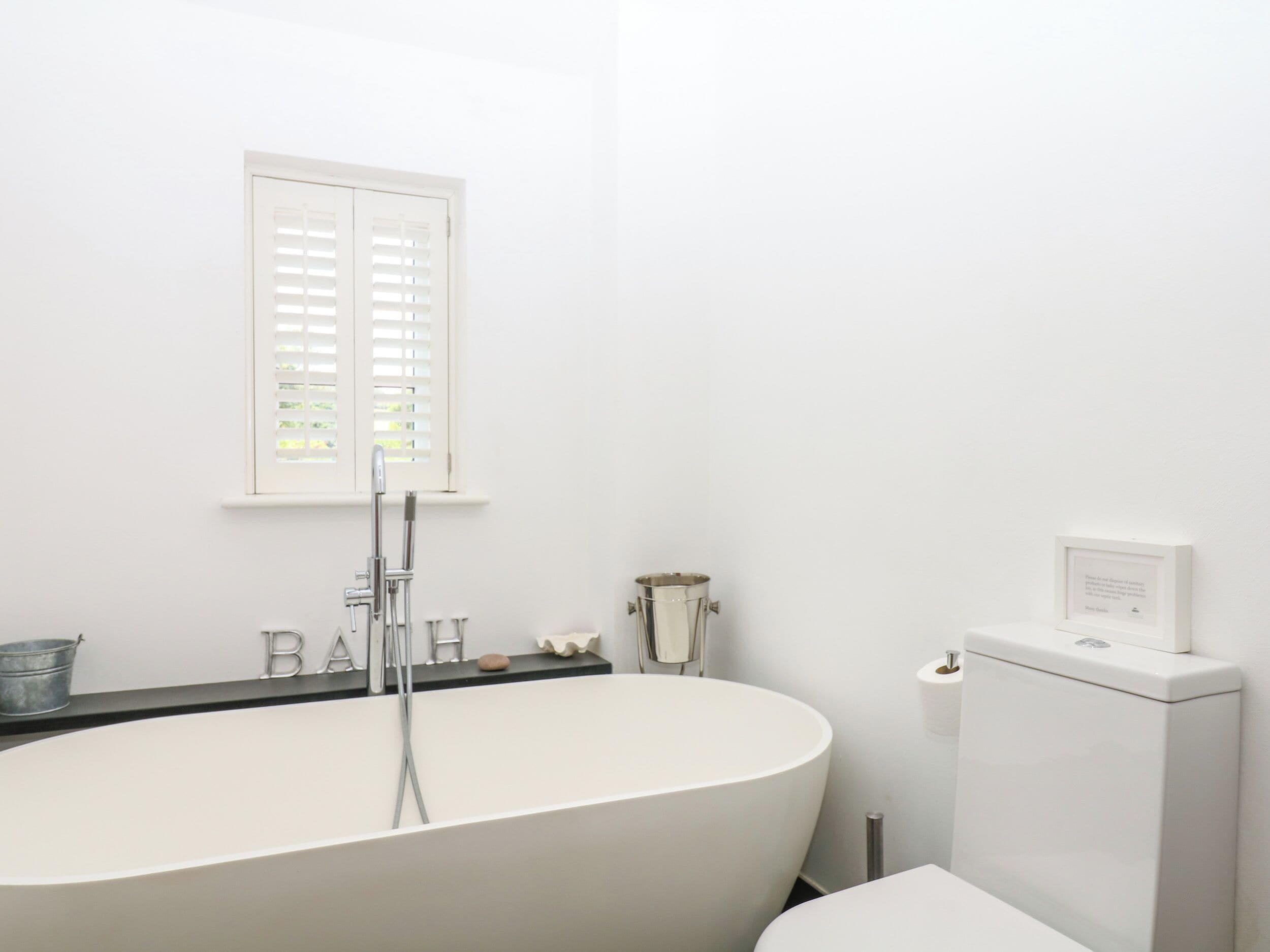 A modern bathroom with a freestanding bathtub, a toilet, and a window with blinds.