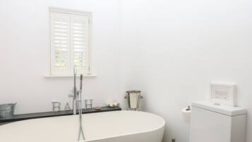 A modern bathroom with a freestanding bathtub, a toilet, and a window with blinds.