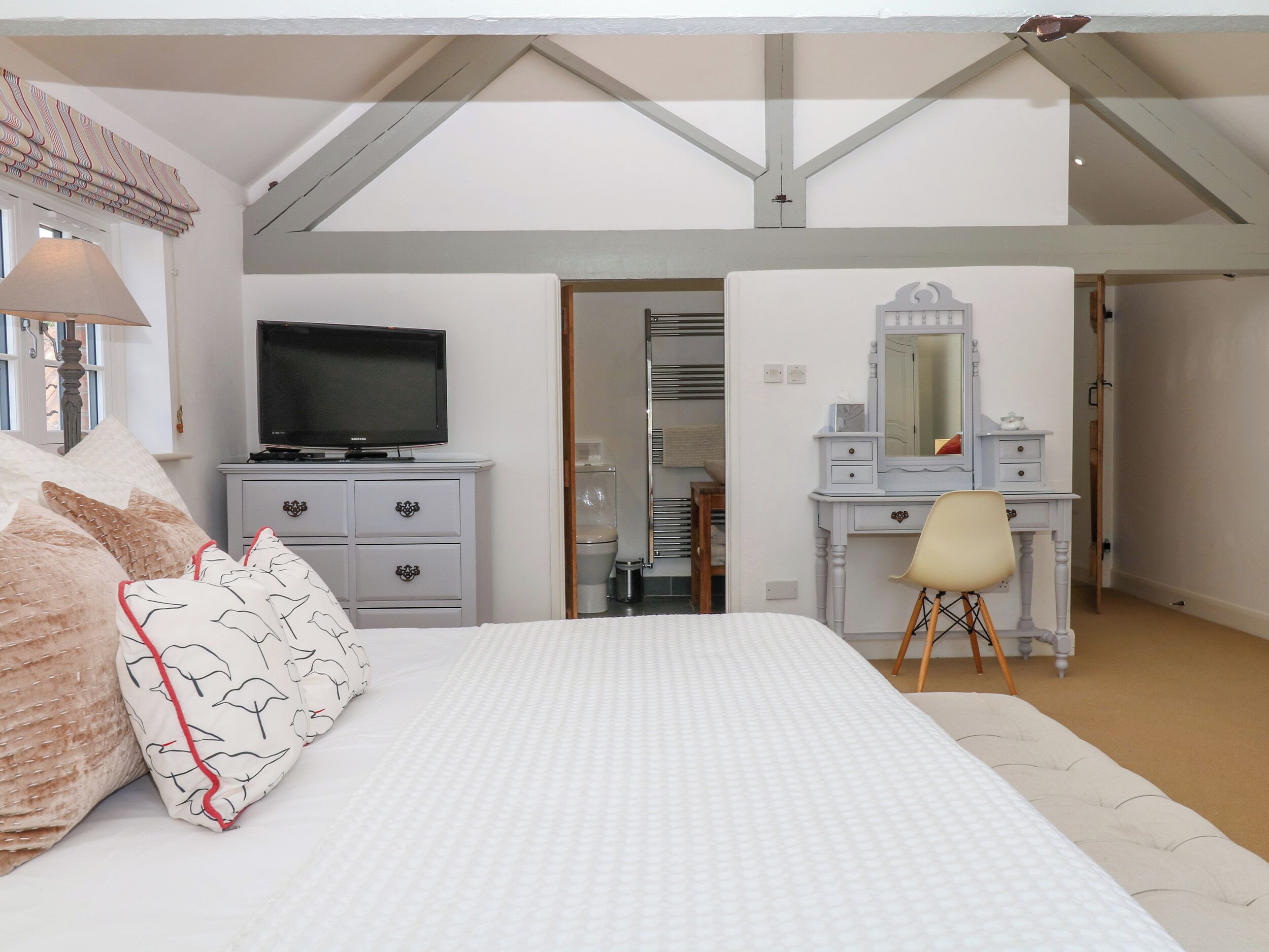 A bedroom with a bed, a television, a dresser, a mirror, and a chair.
