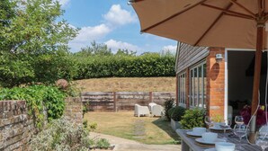 A patio with a table set for dining, a brick wall, and a wooden fence. - Apple Mill (Ottery St Mary)