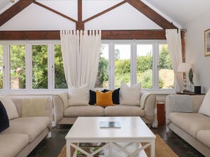 Una habitación con techo alto, vigas de madera a la vista, un conjunto de sofá color beige, una mesa de centro blanca y ventanas amplias con cortinas.