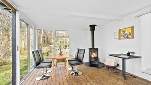 Una habitación acogedora con una mesa de madera, sillas, chimenea y amplios ventanales con vistas al exterior.