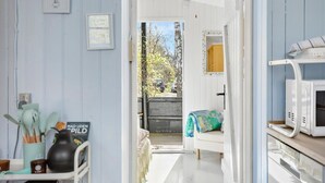 Un pasillo estrecho con una puerta blanca que da a un balcón. Un microondas blanco se encuentra sobre una encimera a la derecha, y un cartel en la pared dice "MAD UDEN SPILD".