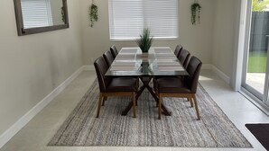 Un coin repas comprenant une table en verre, six chaises, un ventilateur de plafond et deux fenêtres équipées de stores.