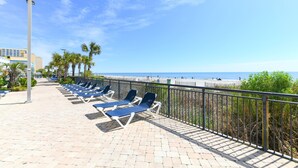 Une promenade en bord de mer, avec des chaises longues, une rambarde et une vue sur la plage et l’océan.