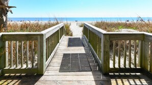 Une promenade en bois qui mène à une plage d’où l’on a une vue dégagée sur l’océan.
