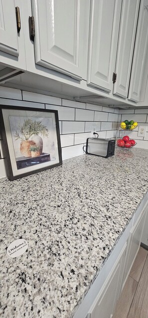 Enjoy cooking in this well-equipped kitchen with a granite countertop, toaster, and ample storage in the white cabinets.