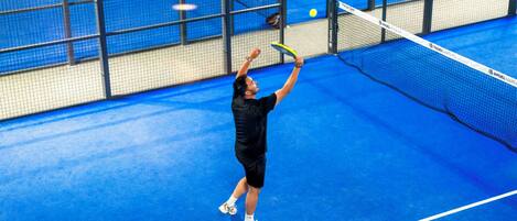 A tennis player in mid-action on a blue indoor court with a net and a ball in play.