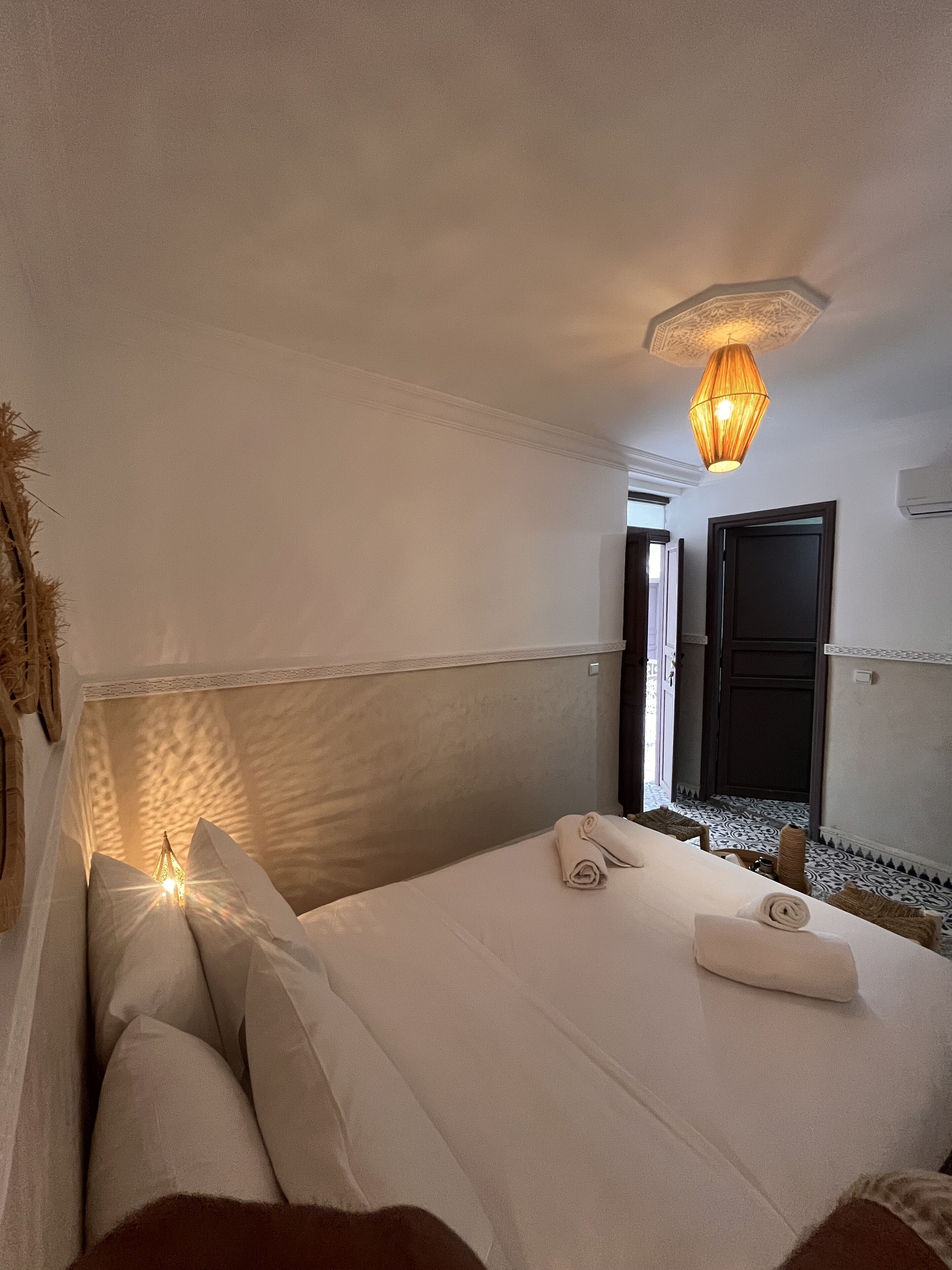 A hotel room with a bed, a hanging light fixture, a door, and a patterned floor.