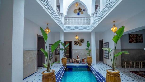 Una piscina interior con suelo de baldosas, rodeada de plantas en macetas y un balcón blanco con iluminación decorativa.