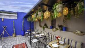 An outdoor dining area with tables and benches, surrounded by potted plants and hanging baskets. - Riad Tarba & spa (Marrakech)