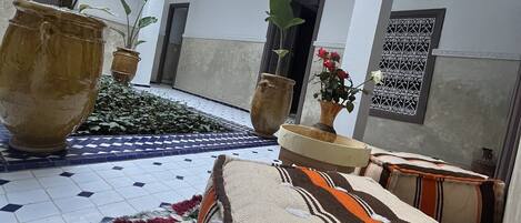 A spacious courtyard with a tiled floor, large potted plants, and a colorful rug.