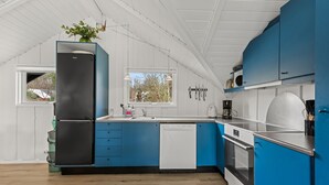Uma cozinha moderna com armários azuis, uma geladeira preta e uma janela com vista para um jardim.