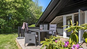 Um pátio externo com móveis de vime, uma mesa e uma porta de vidro que dá para o interior.