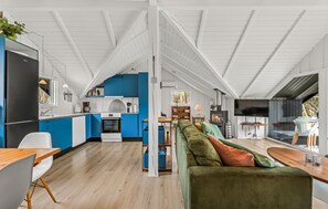 A modern kitchen with blue cabinets, a dining area with a green sofa, and a TV mounted on the wall. - 3 bedroom cozy home in Toftlund (Toftlund)