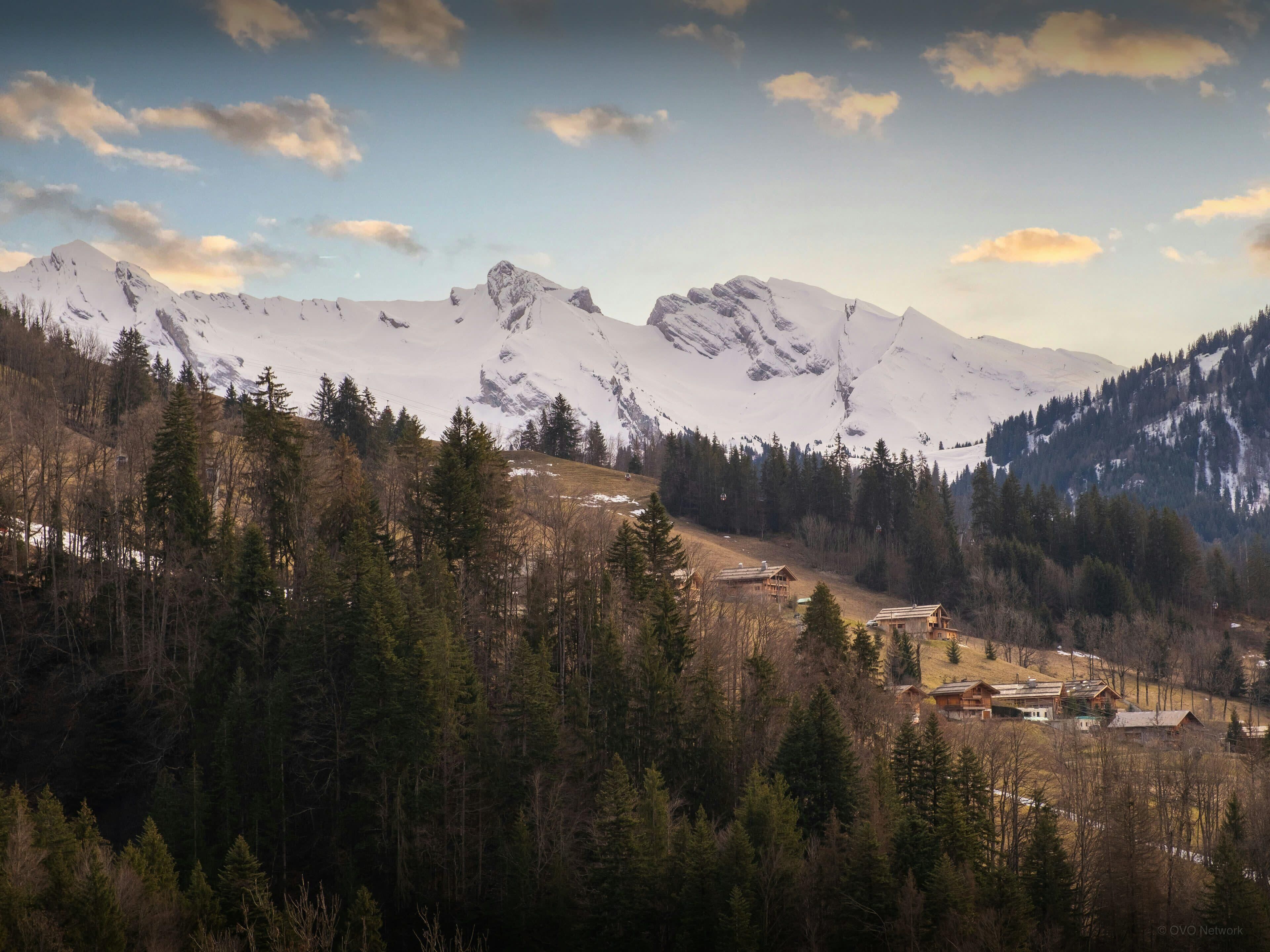 A mountainous landscape with snow-covered peaks and a forested valley.