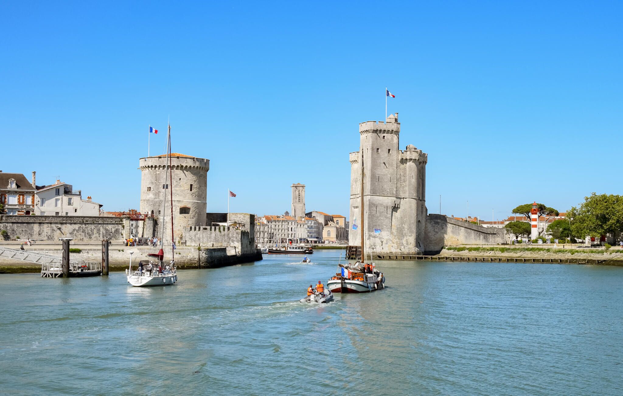 A historic waterfront with two prominent towers, a small boat with passengers, and a clear blue sky.