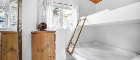 A compact bedroom with a bunk bed, a wooden dresser, a radiator, and a window with curtains.