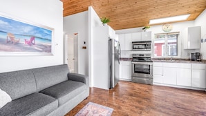 A modern kitchen with white cabinets, stainless steel appliances, and a wooden ceiling.
