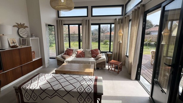 Un salon spacieux comprenant un grand lit, un canapé et une table à manger. De nombreuses fenêtres laissent entrer la lumière naturelle et offrent une vue sur l’extérieur.