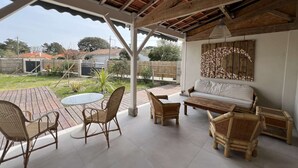 Un espace extérieur aménagé en terrasse, avec un plafond en bois, un canapé blanc, des fauteuils en osier et une table ronde.