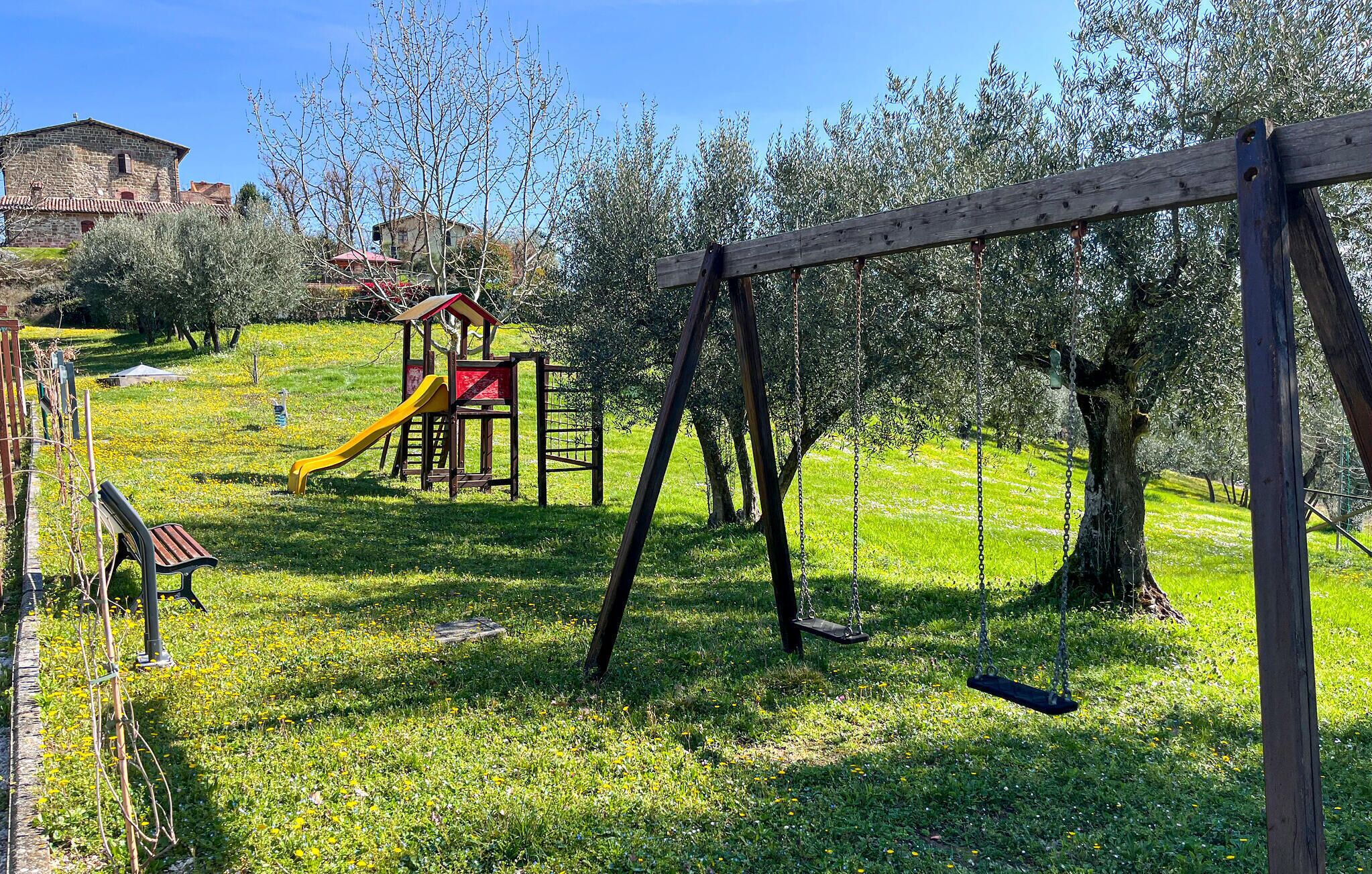 A playground with a slide and swings, surrounded by grass and trees.