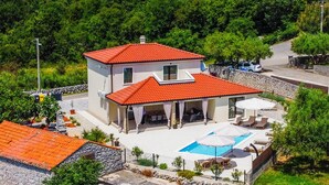 Une maison à deux étages avec un toit recouvert de tuiles rouges, une piscine et un espace salon extérieur.