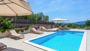 Une piscine entourée d’un mur de pierre et de verdure, avec des chaises longues et des parasols.